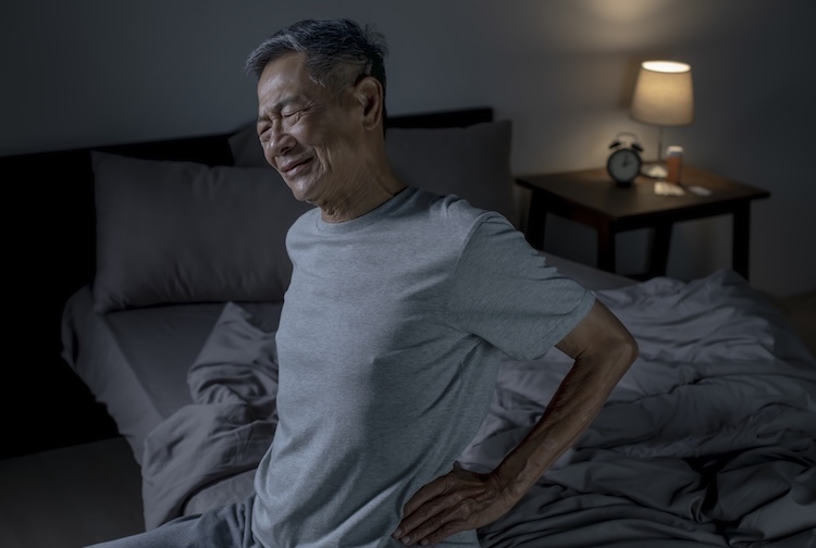 older man gets out of bed after experiencing back pain