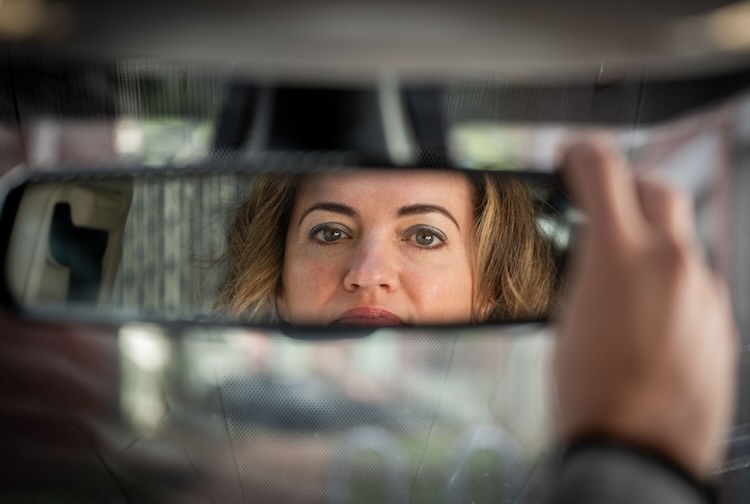 Holly looks in the rearview mirror of her car