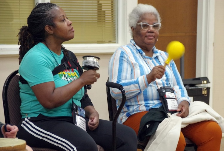 Two women sitting down and playing instruments as part of a camp activity.