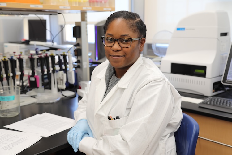 Student in a lab coat sitting at her desk.