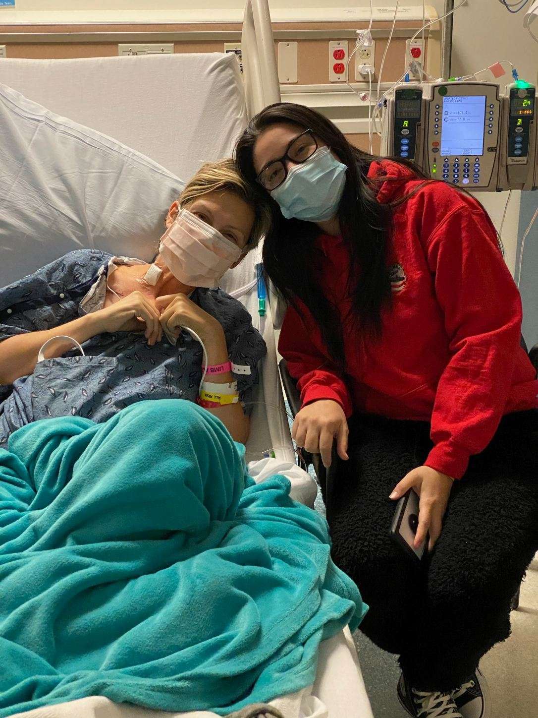 Two women in a hospital room. One woman is sitting on a bed and the other is standing next to her.