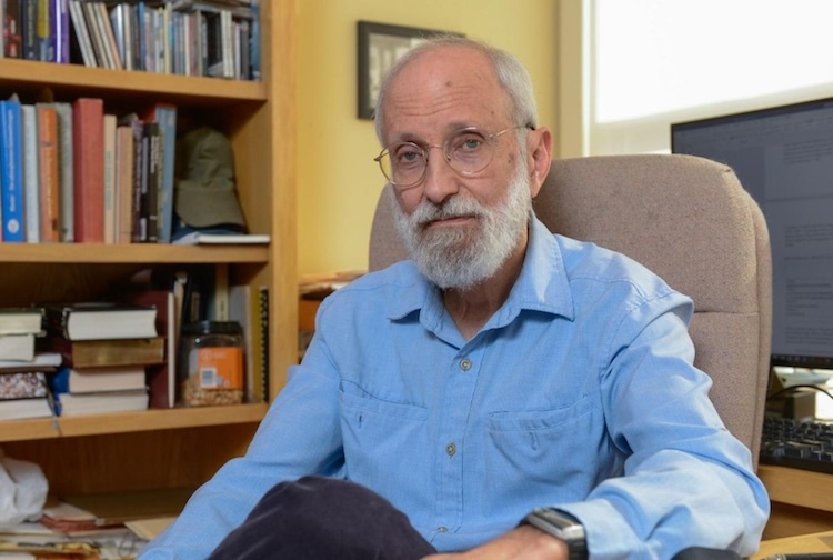 Man sits at desk with bookshelf behind him