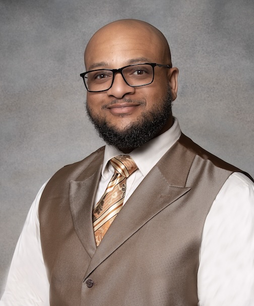 Graduate student in a vest and orange tie sitting for a headshot