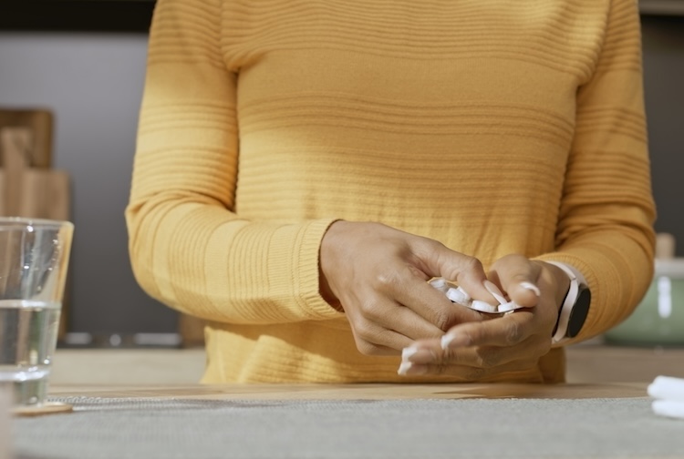 Midsection of woman taking a pill out of a blister pack while standing in a kitchen.