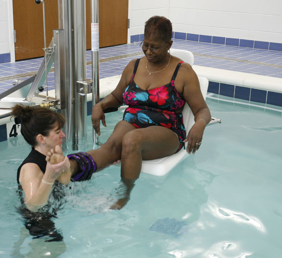 A therapy coach helping a woman perform an aquatic therapy exercise.