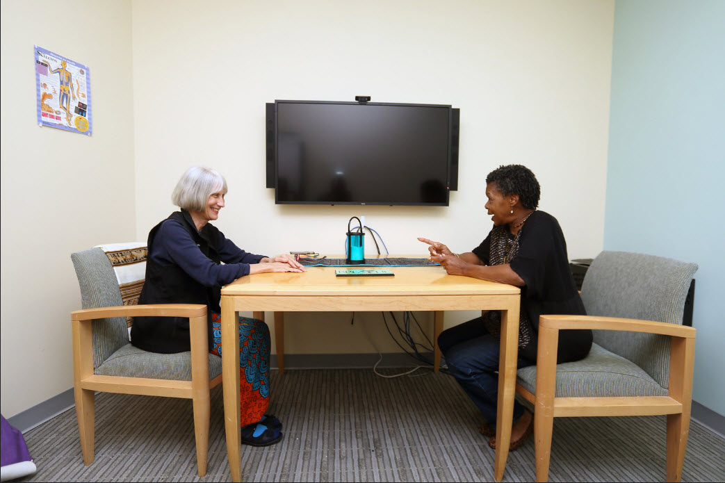 Georgianne Ginder, Certified Health and Wellness Counselor and Holistic Therapist, sitting at table talking to a woman
