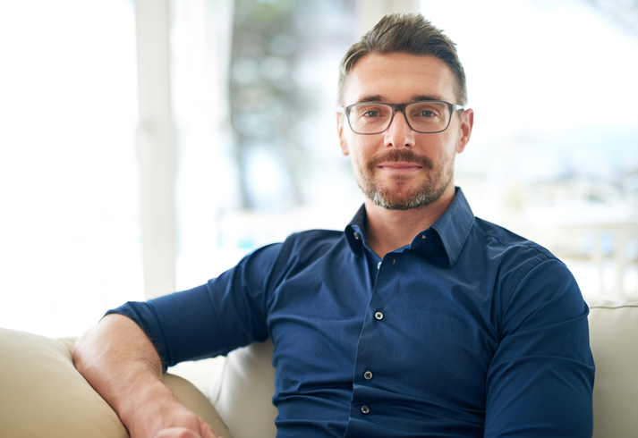 Man wearing glasses sitting on a couch with his arm resting on the arm rest