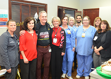 A group of health care workers pose in a break room with balloons and food.
