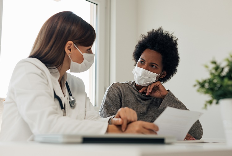 Woman wearing a mask sits next to masked provider holding a piece of paper