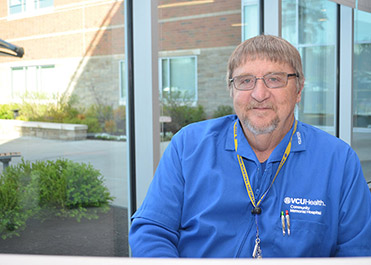 A man wears a blue jacket and sits at a desk in a hospital.