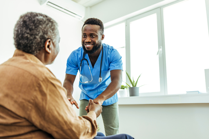 Man in scrubs holding hand of patient and smiling