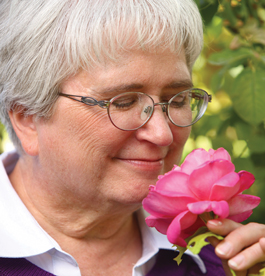 A gray haired, adult woman smelling a flower.