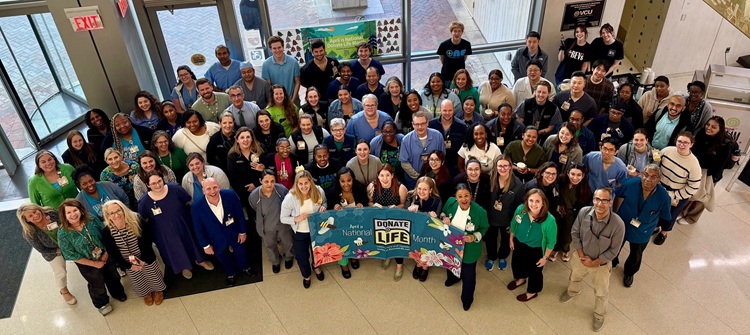 Large group of VCU Health Hume‑Lee Transplant Center team members gathered indoors holding a Donate Life Month banner during April 2026.