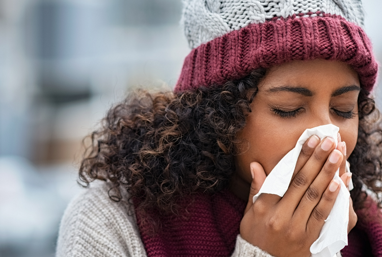 African-American woman wearing a hat and blowing her nose with a tissue