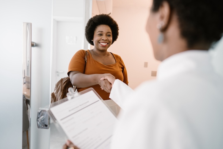 Female patient arriving at doctor’s office, shakes hand with female doctor